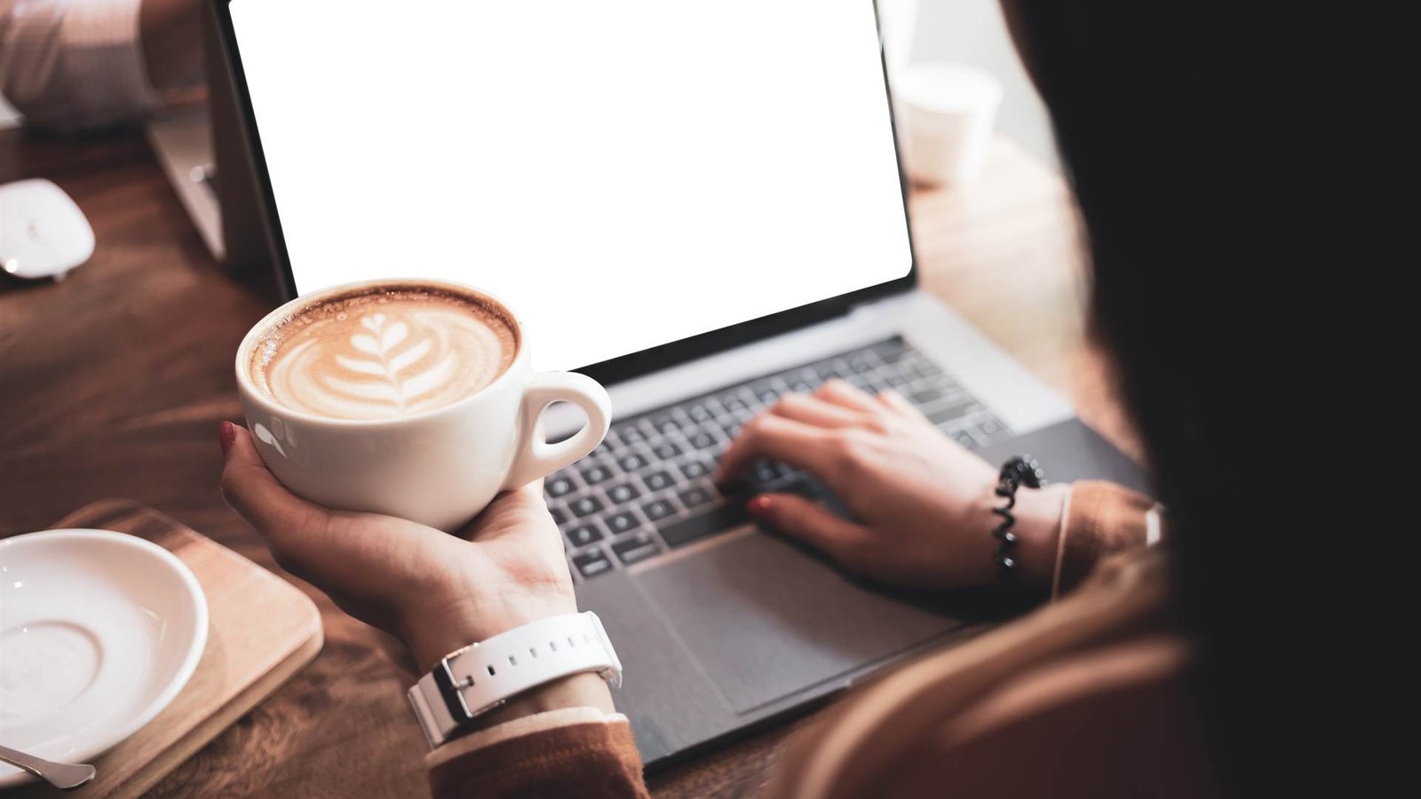 Person with a cup of coffee reading on a laptop
